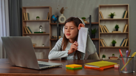 Young child girl studying at home, small girl sits at desk and attends school class online on...