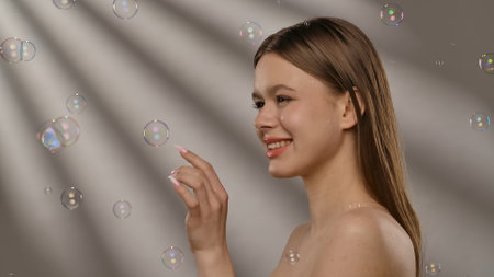 Joyful Woman Surrounded by Floating Soap Bubbles in Soft Lightの写真素材