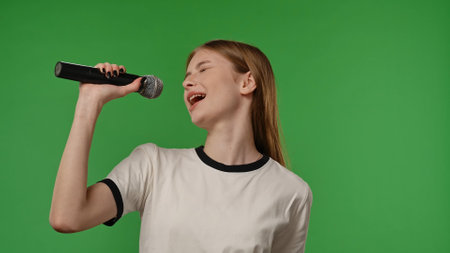 Teenage girl posing at camera smiling and singing song in karaoke microphone, positive expression,...