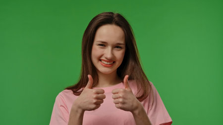 Teenage girl posing at camera smiling and showing thumb up like gesture, positive expression,...