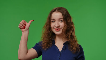 Teenage girl posing at camera smiling and showing thumb up like gesture, positive expression, isolated on chroma key green screen studio background mockup.の写真素材
