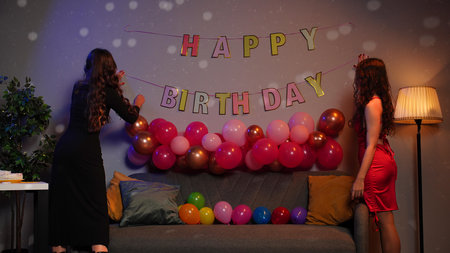 Teenagers birthday party, girls decorate room for surprise party, hanging balloons and letters on the wall. Happy group of young people having fun together.の写真素材
