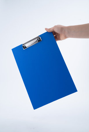 Hand Holding a Blue Clipboard Against White Backgroundの写真素材