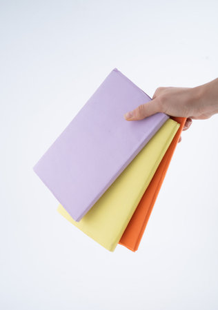 Hand Holding Three Colorful Books in a Simple Settingの写真素材