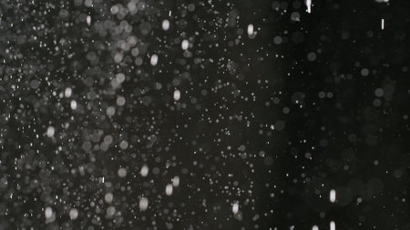 Many bright dust particles of white powder in low light on empty dark black contrast background.