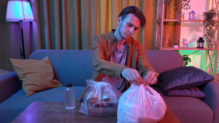 Young man sitting at home in evening on the sofa, ordered delivery of tasty asian food, put packages...