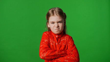 Little girl child with pouting face and crossed arms looks at camera, isolated on chroma key green screen studio background mockup.の写真素材