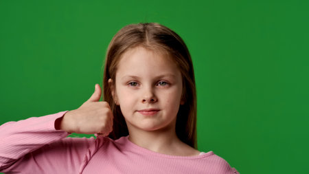 Smiling girl child looks at camera and shows thumb up hand sign, positive expression, isolated on chroma key green screen studio background mockup.の写真素材