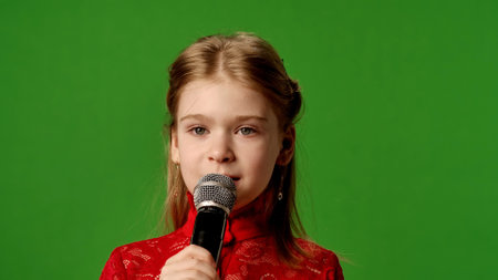 Smiling girl child singing song in karaoke microphone, positive expression, isolated on chroma key...