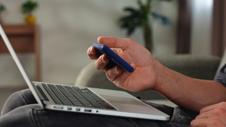 Person Using Smartphone and Laptop Simultaneously at Homeの写真素材