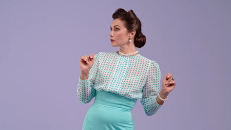 Young woman in vintage outfit and with glamorous hairstyle poses on purple studio background.の写真素材