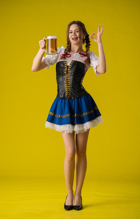 Woman Celebrating with Beer in Festive Attire Against Yellow Backgroundの写真素材