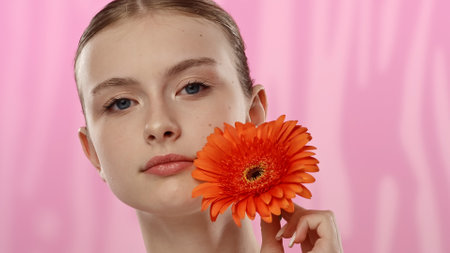 Young Woman with Bright Orange Flower on Vibrant Backgroundの写真素材