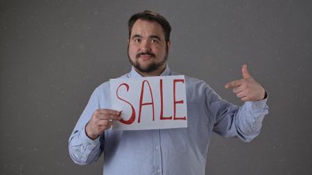 Man Holding Sale Sign Pointing Enthusiastically at Discount Eventの写真素材