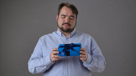 Man Examining Gift Box with Blue Ribbon in Curiosityの写真素材