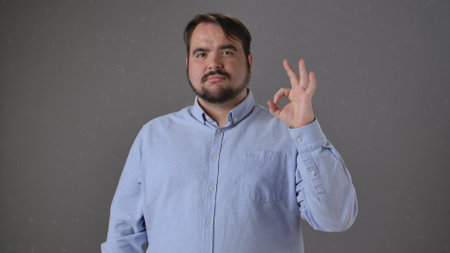Man Gesturing OK in Light Blue Shirt with Neutral Backgroundの写真素材