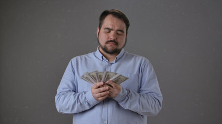 Man Holding Dollar Bills with Confident Expression in Grey Backgroundの写真素材