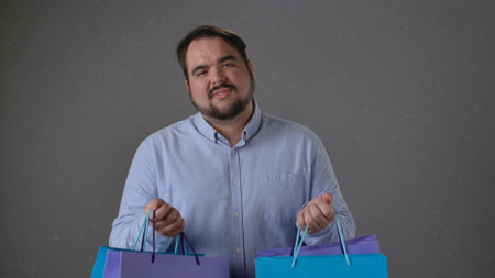 Man Holding Shopping Bags in Front of Grey Backgroundの写真素材