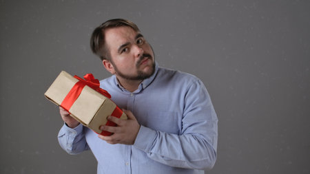 Man Examining Gift Box with Red Ribbon in Curiosityの写真素材