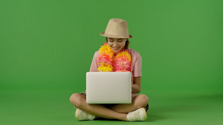 Smiling Young Woman with Laptop and Bright Lei on Green Backgroundの写真素材