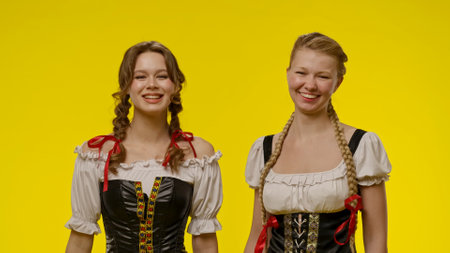 Two women smiling in traditional costumes against yellow backgroundの写真素材