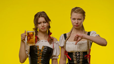 Two women in traditional dress with mixed emotions and beerの写真素材
