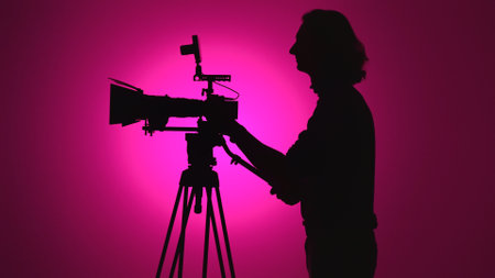 Silhouette of Filmmaker Operating Camera on Tripod with Pink Background