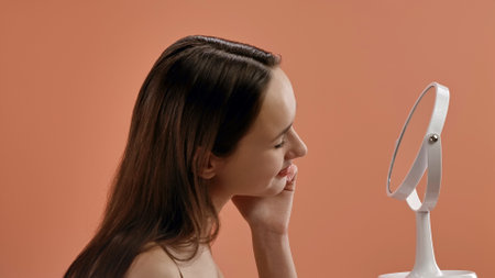 Woman Gently Touching Her Skin in Front of Mirrorの写真素材