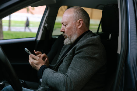 Elderly man behind the wheel of a car looking at information on a smartphone