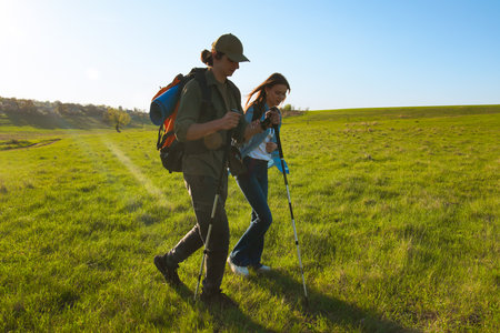 Young Couple Hiking with Trekking Poles in Open Green Fieldの写真素材