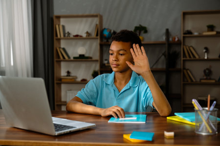 Young african american child boy studying at home, kid sits at desk attends school class online on...