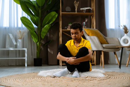 Contemplative Young African American Child Boy Sitting on a Cozy Carpet at Homeの写真素材