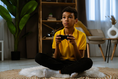 Young african american child boy spending free time at home, kid sits on the floor in the living...