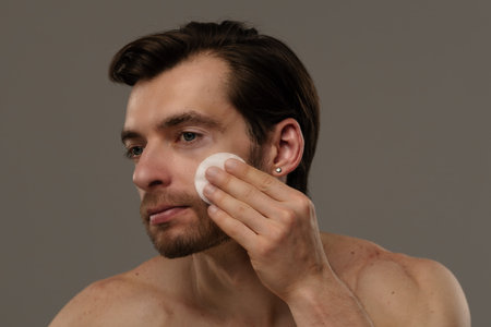 Man Cleansing Face with Cotton Pad under Soft Lightingの写真素材