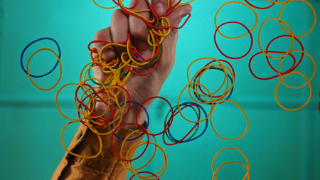 Hand Holding Colorful Elastic Bands Against Blue Backgroundの写真素材