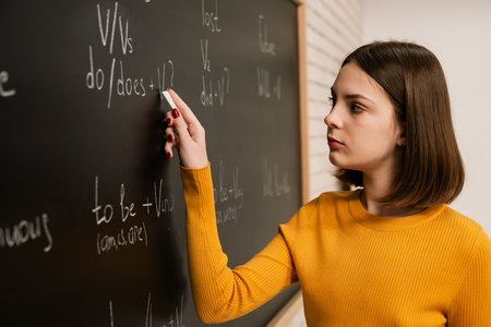 Young Woman Writing Equations on Chalkboard in Classroomの写真素材
