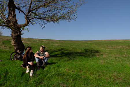 Young Couple Relaxing Under a Tree in a Vast Green Fieldの写真素材