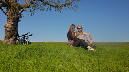 Young Couple Relaxing Under a Tree in a Vast Green Fieldの写真素材