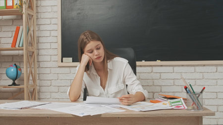 Young woman college teacher at desk in classroom in front of chalkboard checking homework, tires expression taking nap at the table. Education concept.の写真素材