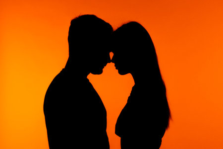 Silhouette of Couple in Intimate Pose Against Orange Backgroundの写真素材