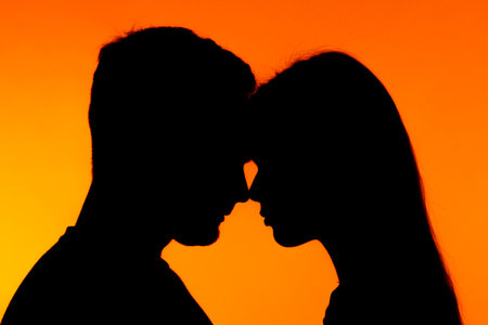 Silhouette of Couple in Intimate Pose Against Orange Backgroundの写真素材