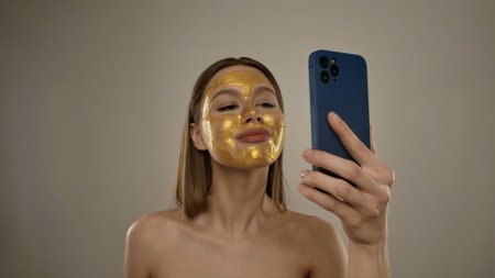 Woman Taking Selfie with Gold Face Mask on Phoneの写真素材