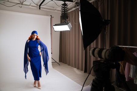 Young adult woman spending time at studio, woman model in fancy outfit taking part in a photoshoot in professional studio with photographer and assistants.の写真素材