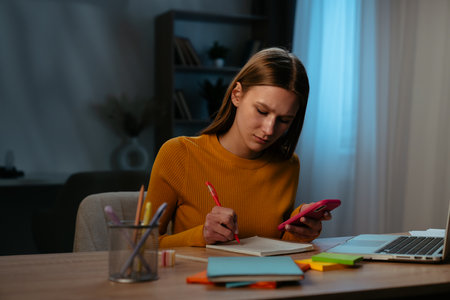 Young Woman Using Smartphone While Working at Home Office Deskの写真素材