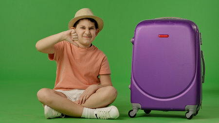 Displeased Child with Purple Suitcase on Green Backgroundの写真素材