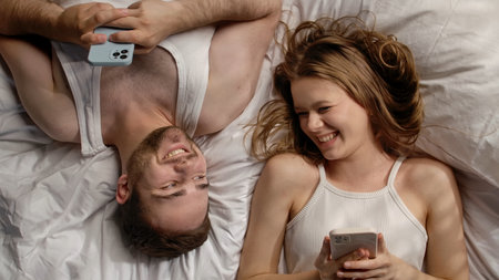 Joyful Couple Relaxing Together with Smartphones at Homeの写真素材