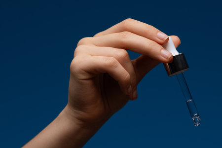 Hand Holding Cosmetic Dropper with Liquid on Blue Backgroundの写真素材