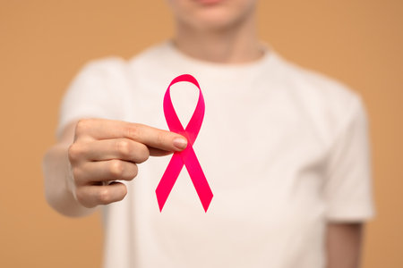 Pink Ribbon Held in Hand Signifying Breast Cancer Awarenessの写真素材