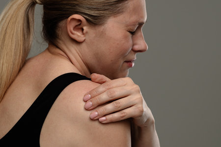 Woman Experiencing Shoulder Pain with Visible Discomfortの写真素材