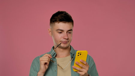 Young Man With Yellow Phone Pondering on Pink Background